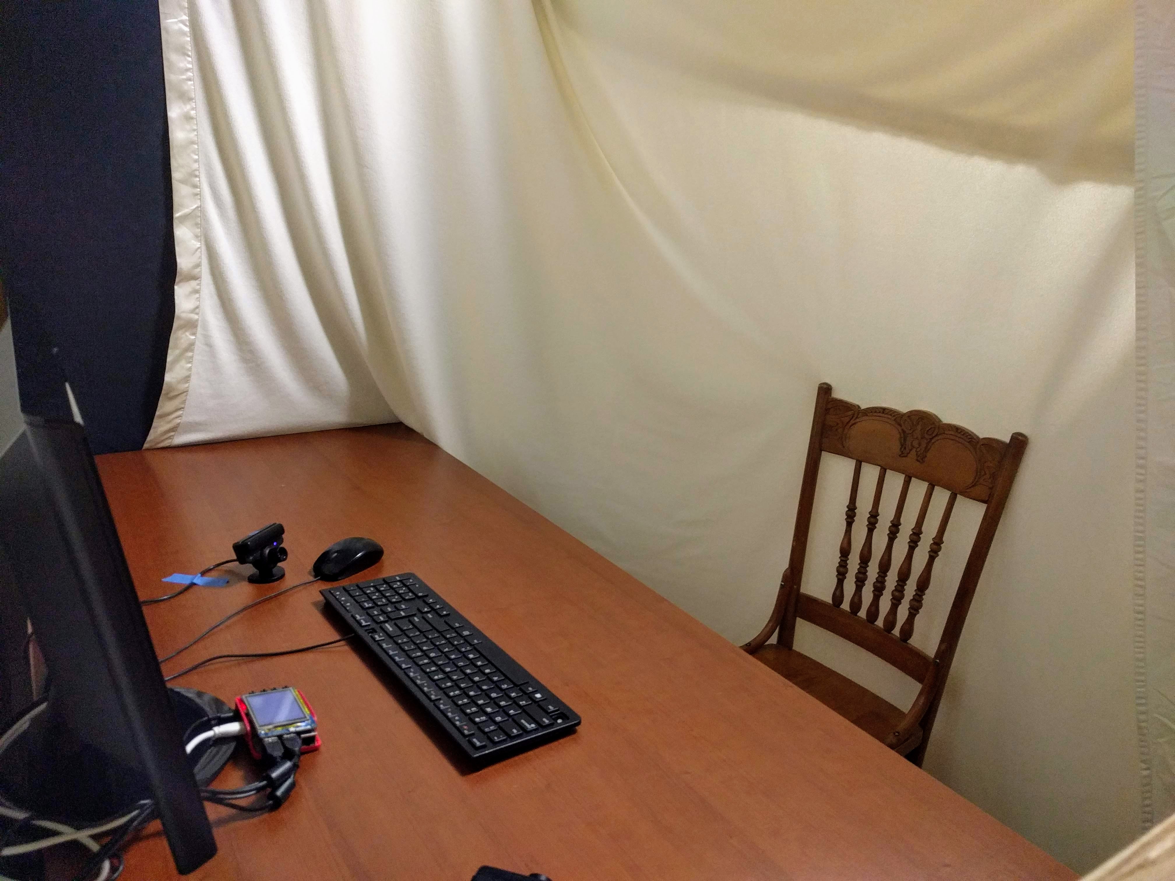 Theremin playing station atop a desk with white blanket hanging behind desk chair to provide neutral background