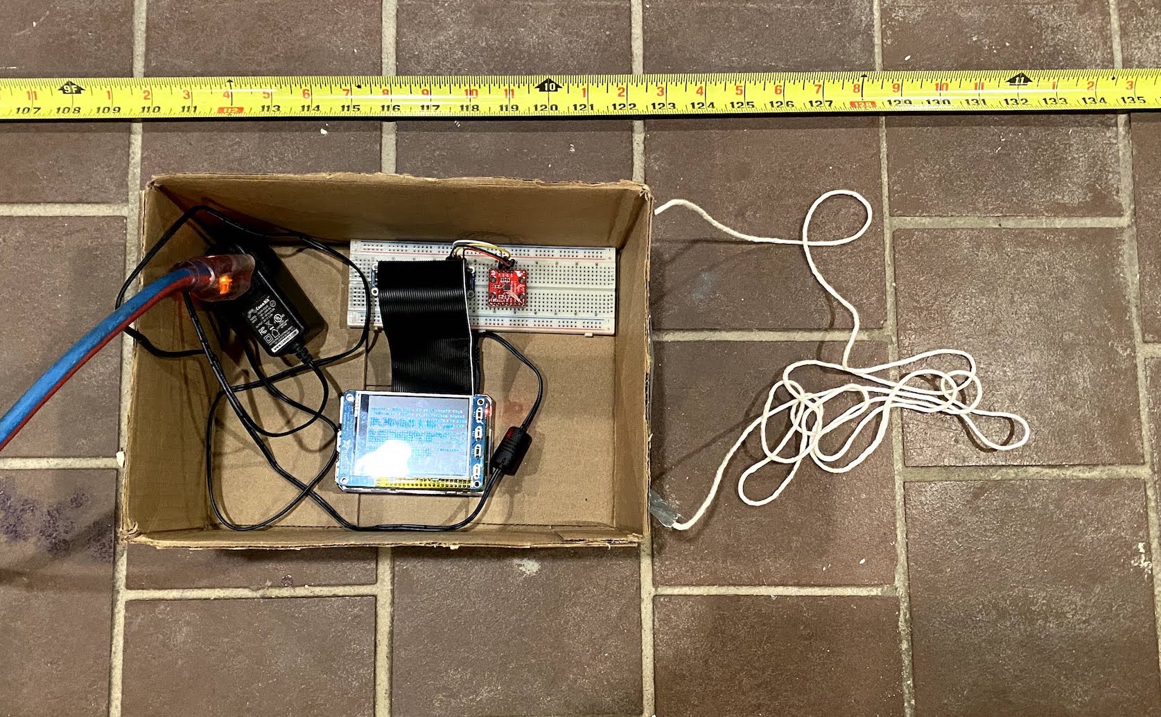 Raspberry Pi laying in a cardboard box next to a tape measure